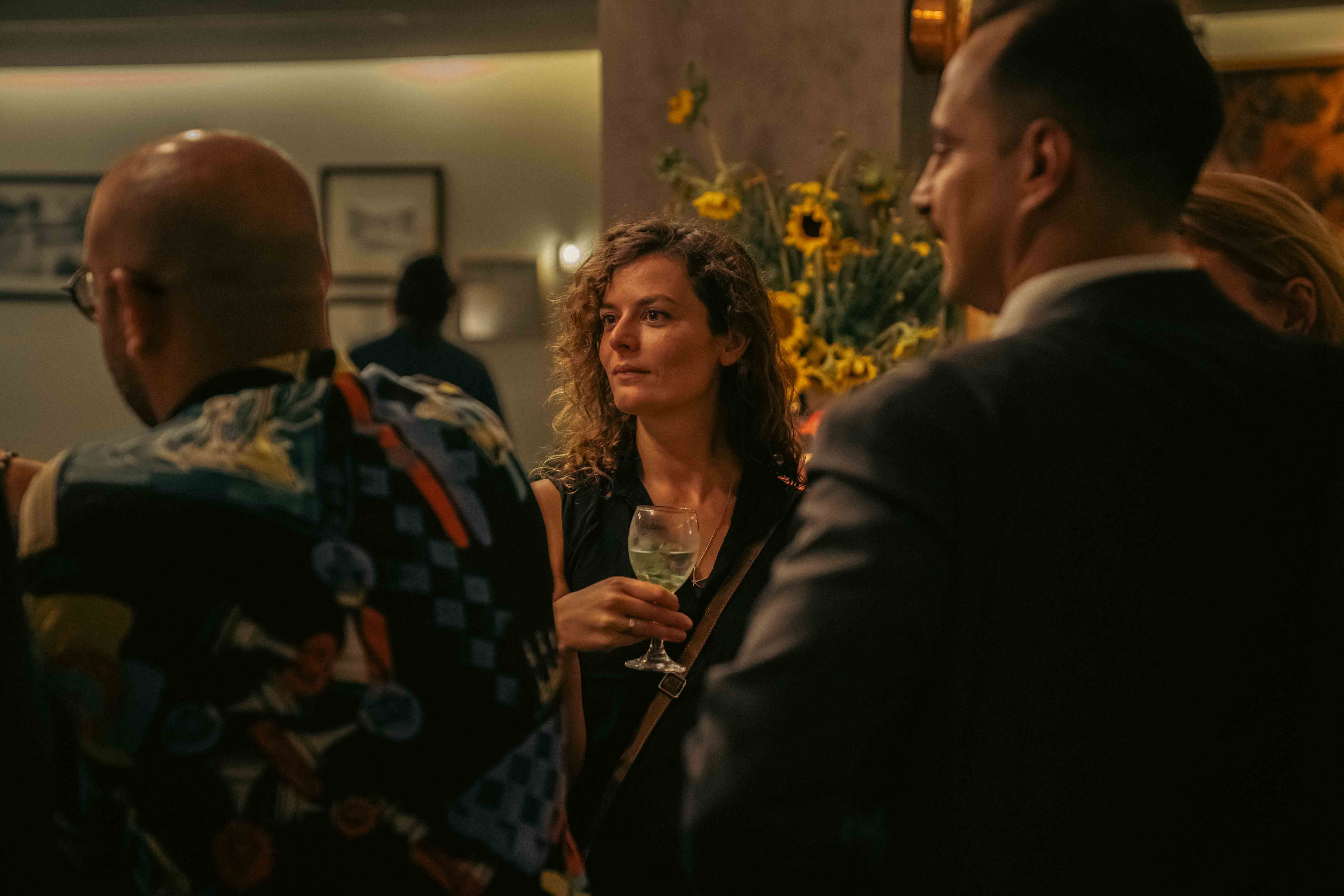 Guests mingling over drinks beside a vase of sunflowers