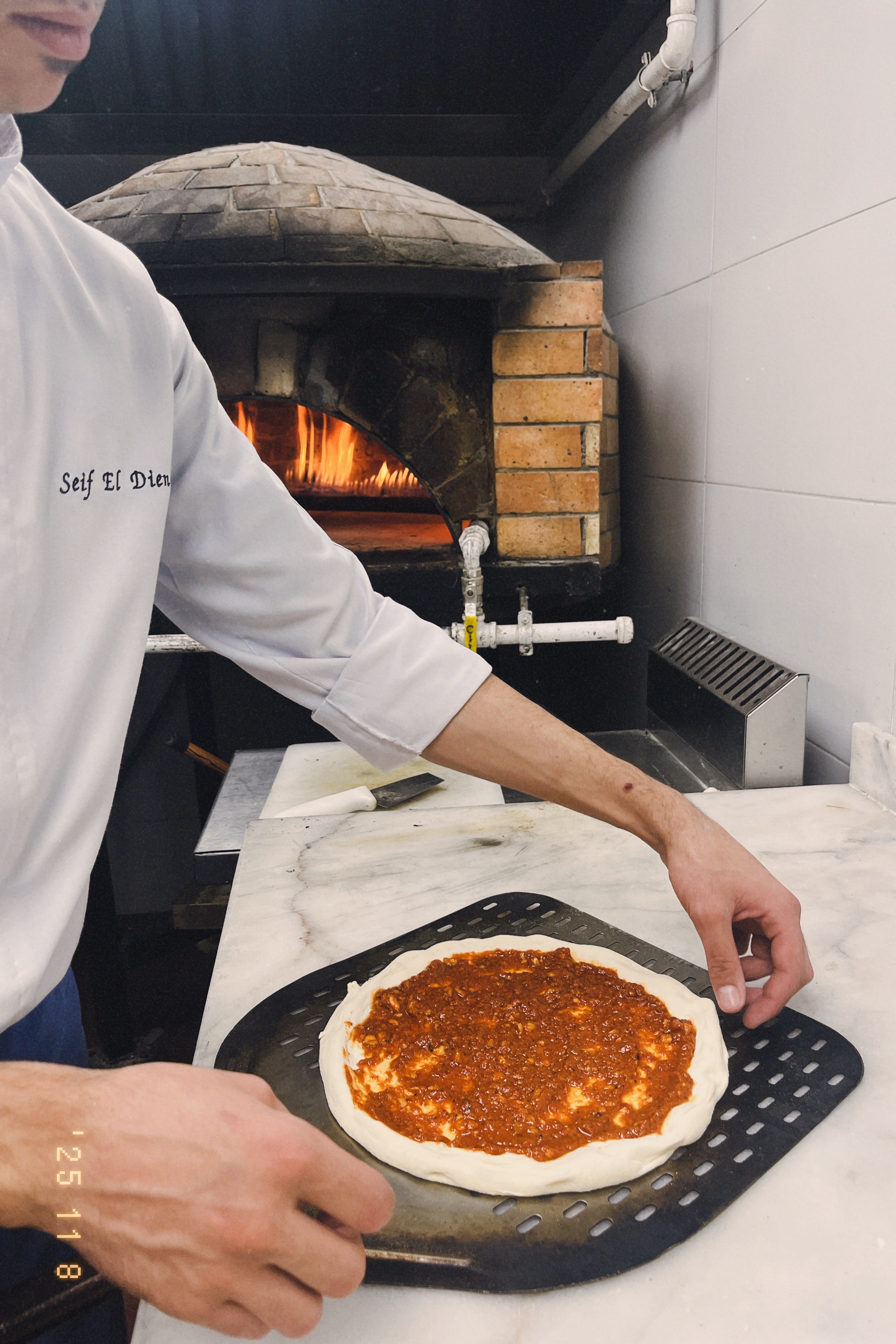A chef building a pizza beside Almería's wood-fired brick oven